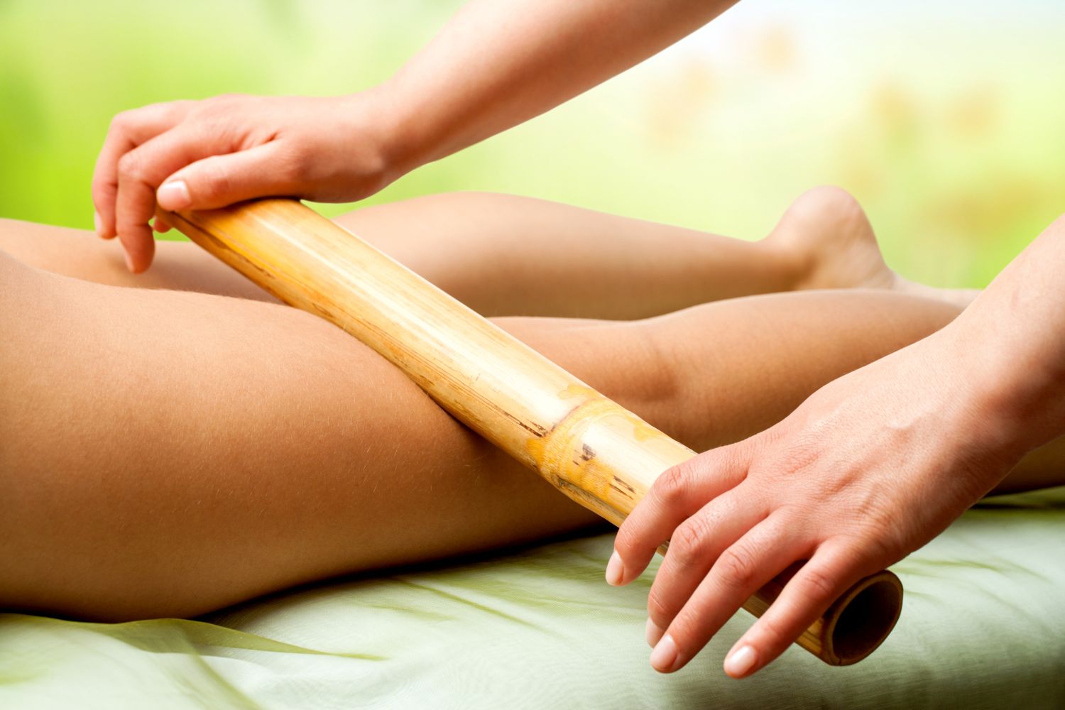 Hands massaging female legs with bamboo.